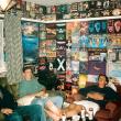 Молодые люди отдыхают в оклеенной флаерами вечеринок комнате. 90-е годы 