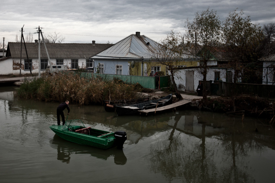 Лодка отчаливает от берега на одном из каналов в Вилково. Город расположен в устье Дуная, вдоль улиц прорыты многочисленные каналы, еще 50 лет назад лодка была более распространенным транспортным средством, чем машины. Сейчас многие каналы обмелели или засыпаны
