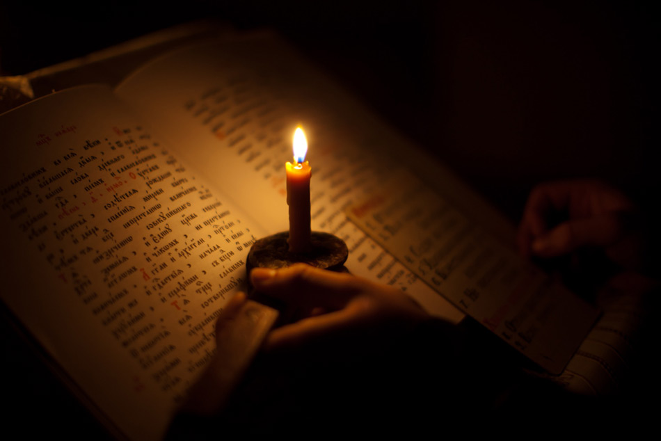Послушник читает при свете свечи