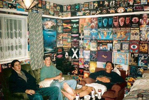 Молодые люди отдыхают в оклеенной флаерами вечеринок комнате. 90-е годы 