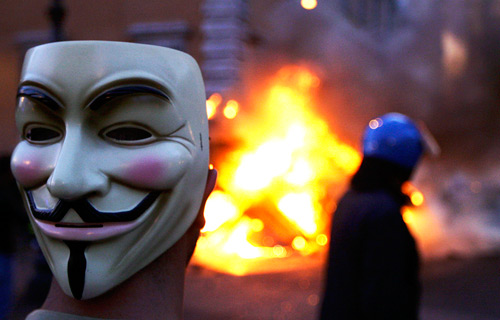 Протестующий в маске Гая Фокса на фоне горящей машины полицейских во время всемирной акции протеста. 15 октября 2011. Рим, Италия