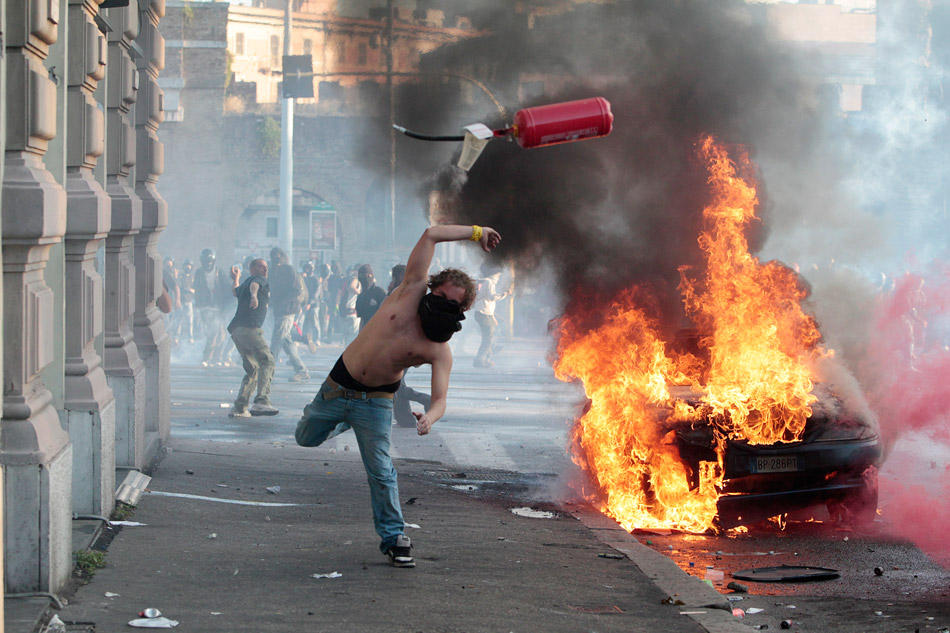 Рим (Италия). Протестующий бросает огнетушитель в полицейских во время уличных беспорядков в Риме. 15 октября 2011 года